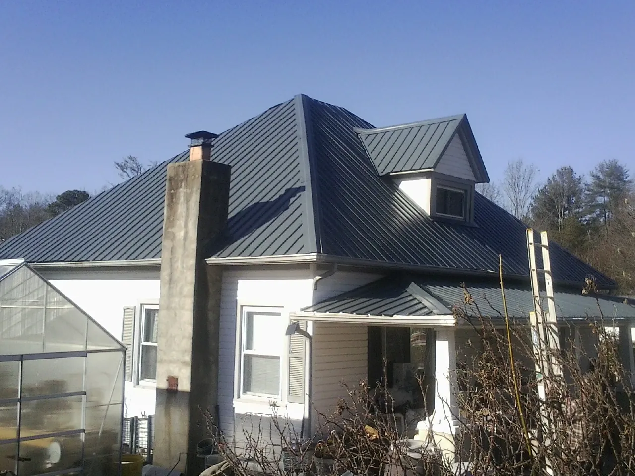 Dark blue standing seam metal roof on a white farmhouse with dormer — Slate & Tile Roof Repair by Roofing Brothers in Forest Park