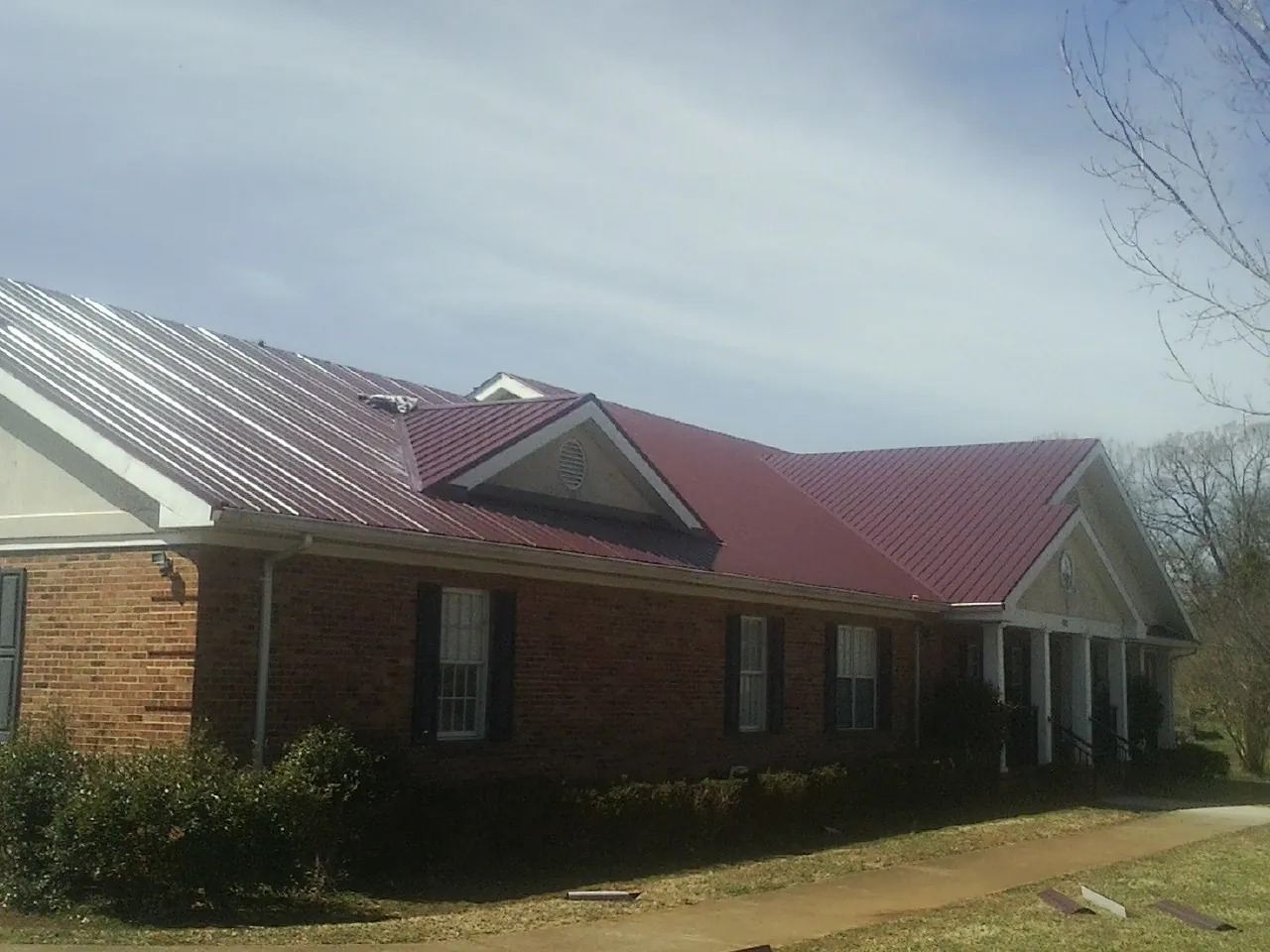 Red metal roof with gabled entries on a long brick building, from a Hail Damage Roof Repair job in Forest Park