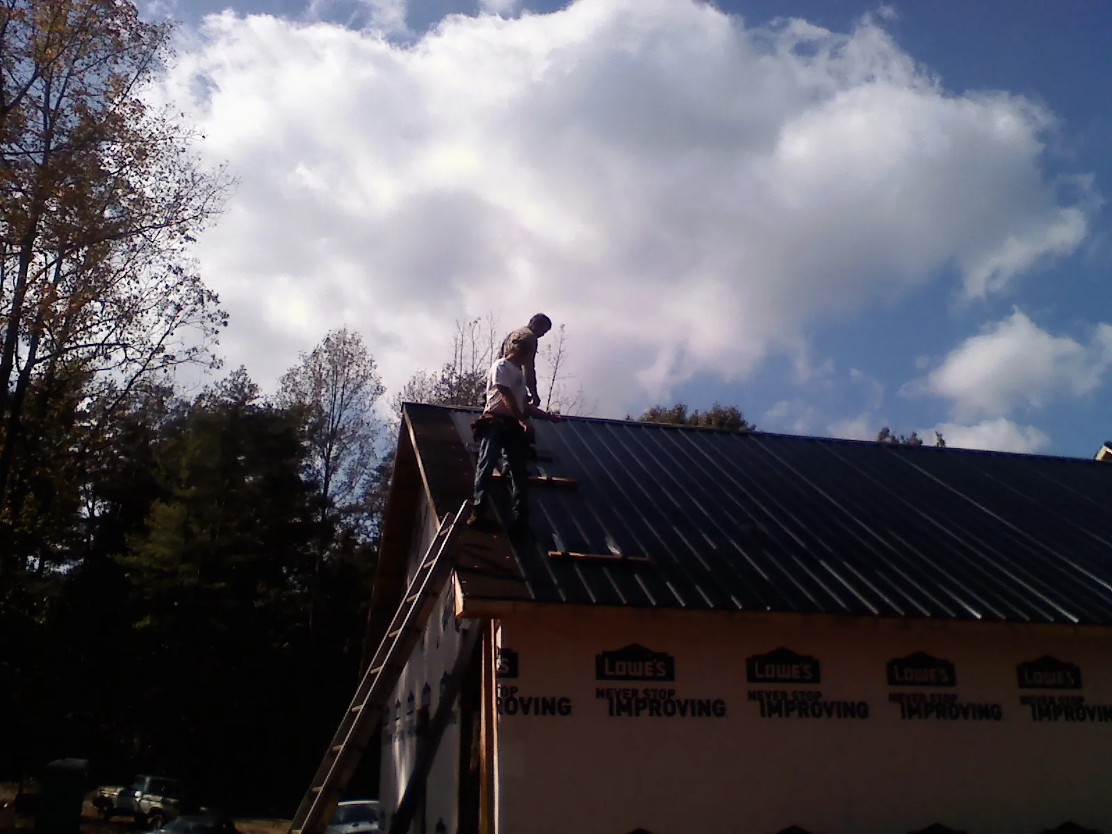 Roofer fastening dark metal panels high against a cloudy sky, from a Roof Inspection job in Forest Park