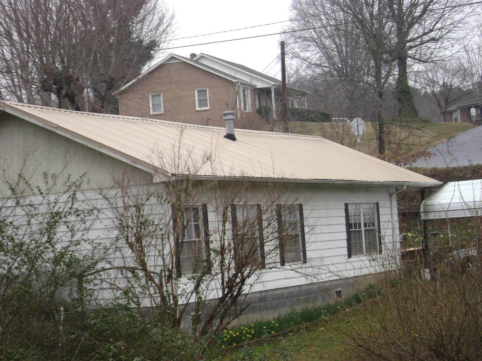 Tan metal roof on a white sided house set into a hillside — Commercial Roofing by Roofing Brothers in Forest Park